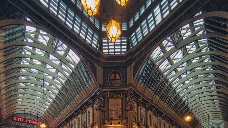 An ornate arched glass-and-ironwork ceiling of a covered Victorian market, with hanging lantern lights