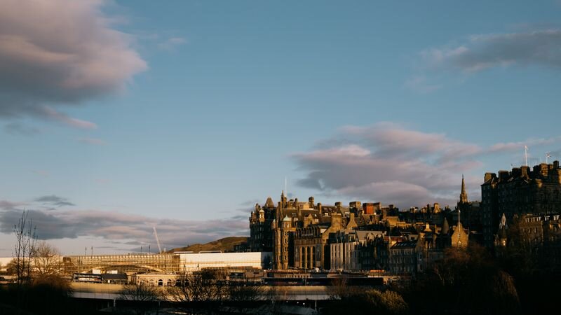 A hillside old-town skyline of stone spires and rooftops catching golden evening light beneath a pastel sky