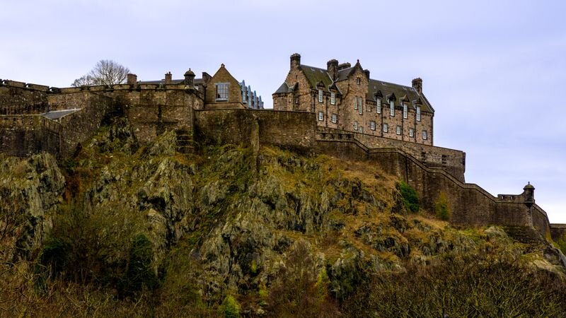 A stone castle with turrets perched atop a rocky, tree-lined crag