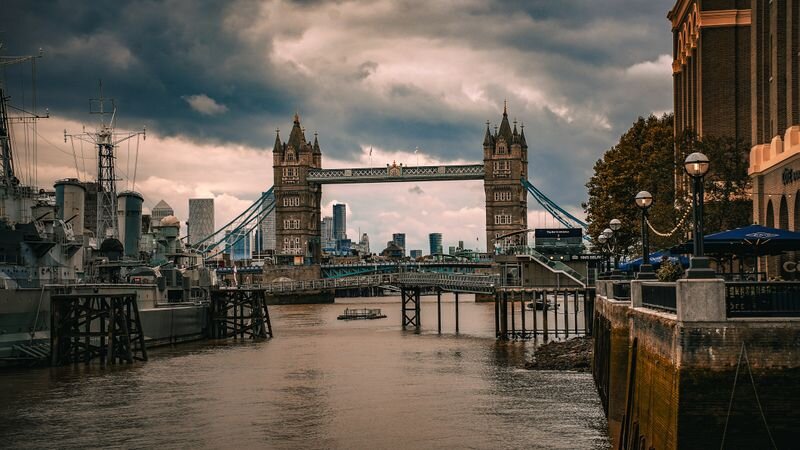 Tower Bridge's twin stone towers spanning the River Thames, with a docked warship in the foreground